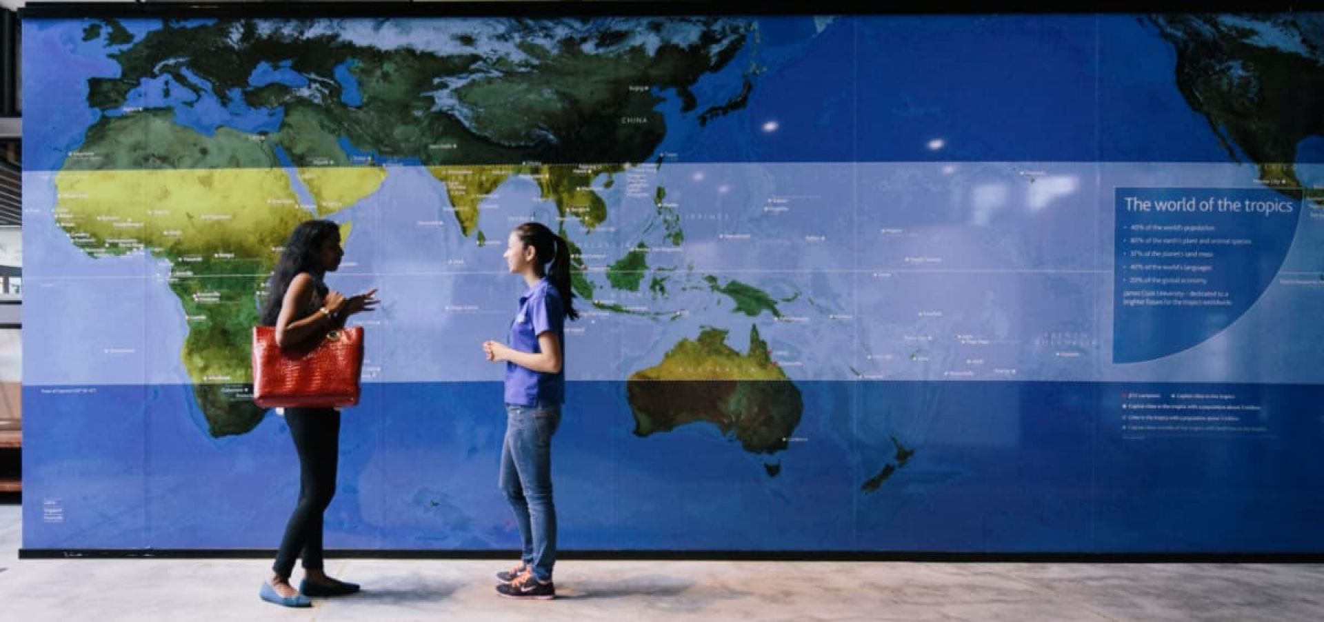 Two students chatting in front of a map of the Tropics