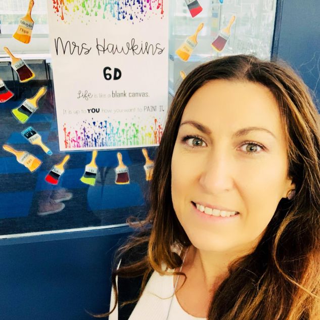 Year Six teacher Courtney Hawkins smiling and standing in front of a classroom door with a sign saying 'Mrs Hawkins 6D'. 