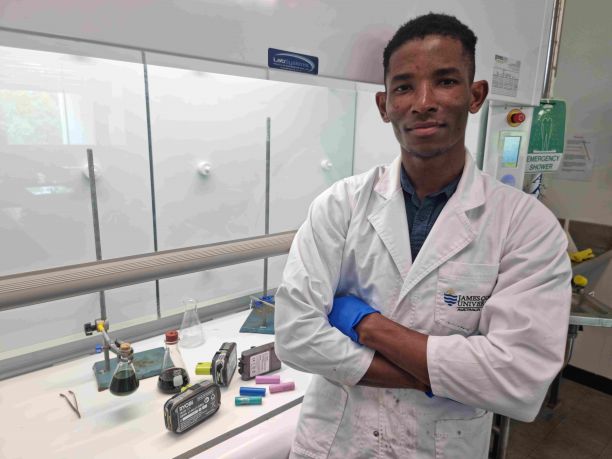 JCU PhD Candidate Emenike Okonkwo smiling with his arms crossed and standing in front of a laboratory bench with science equipment. 