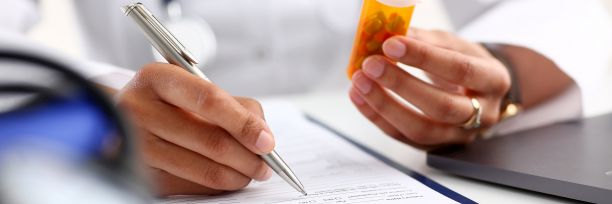 person writing on paper while holding a pill bottle