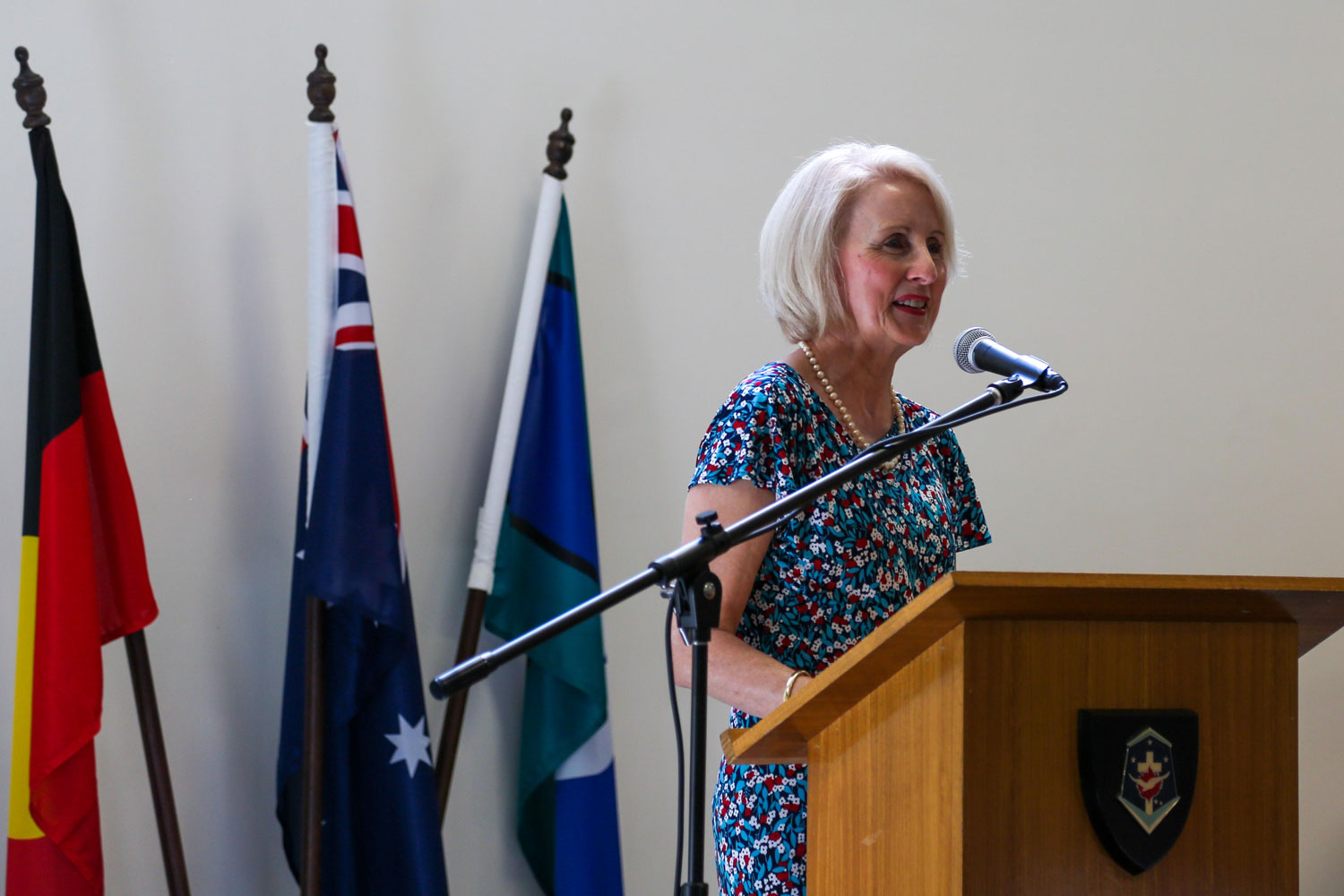 a woman stands at a lectern, The Australian, Aboriginal, and Torres Strait Islander flags behind her
