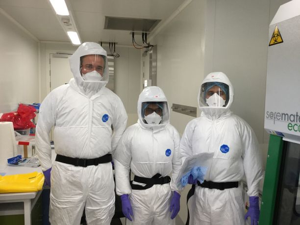 Three men in biohazard suits in lab