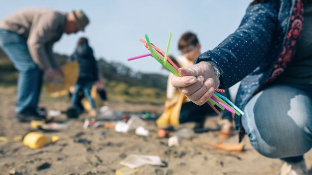 Woman picking up plastic rubbish and straws on a beach