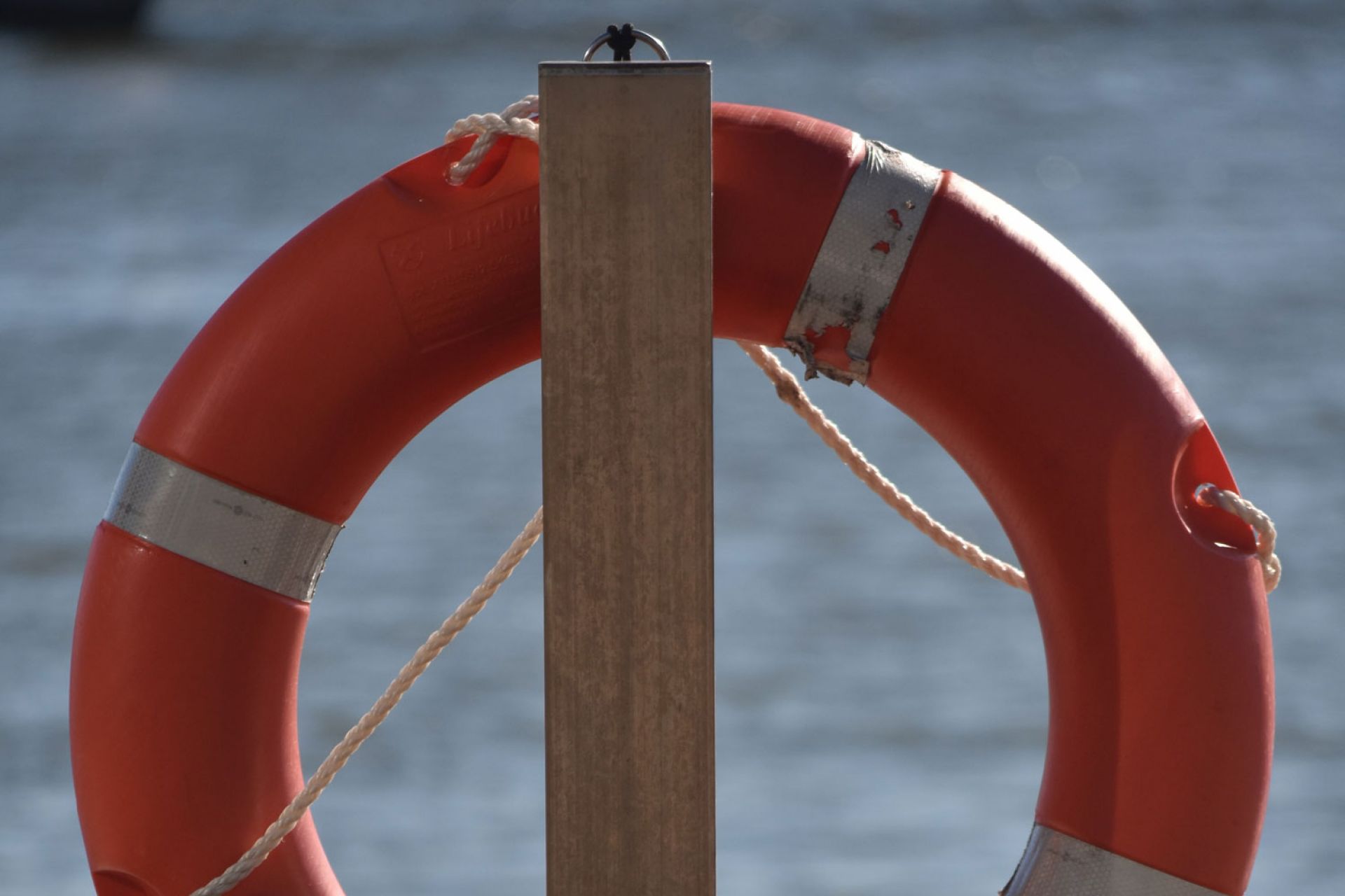 Cropped image of an orange life buoy fixed to a post, water behind 