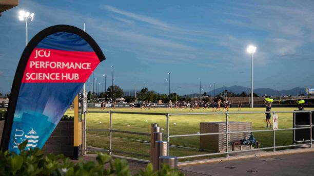 Training field outside the Cowboys centre in the evening with players on the field and a banner to the left that says JCU Performance Science Hub. 