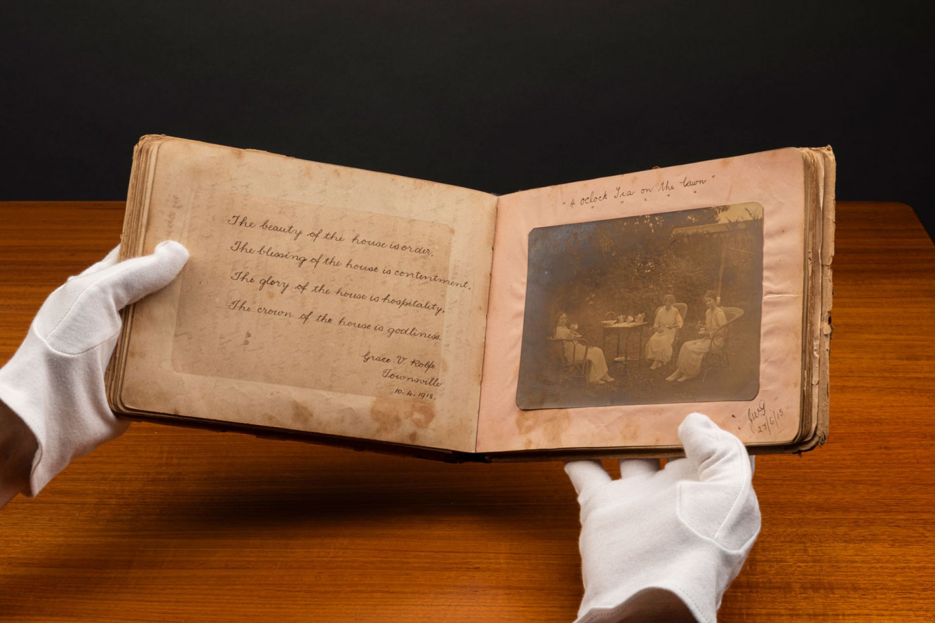 gloved hands open an old book to show an inscription on one side, and a photo on the other