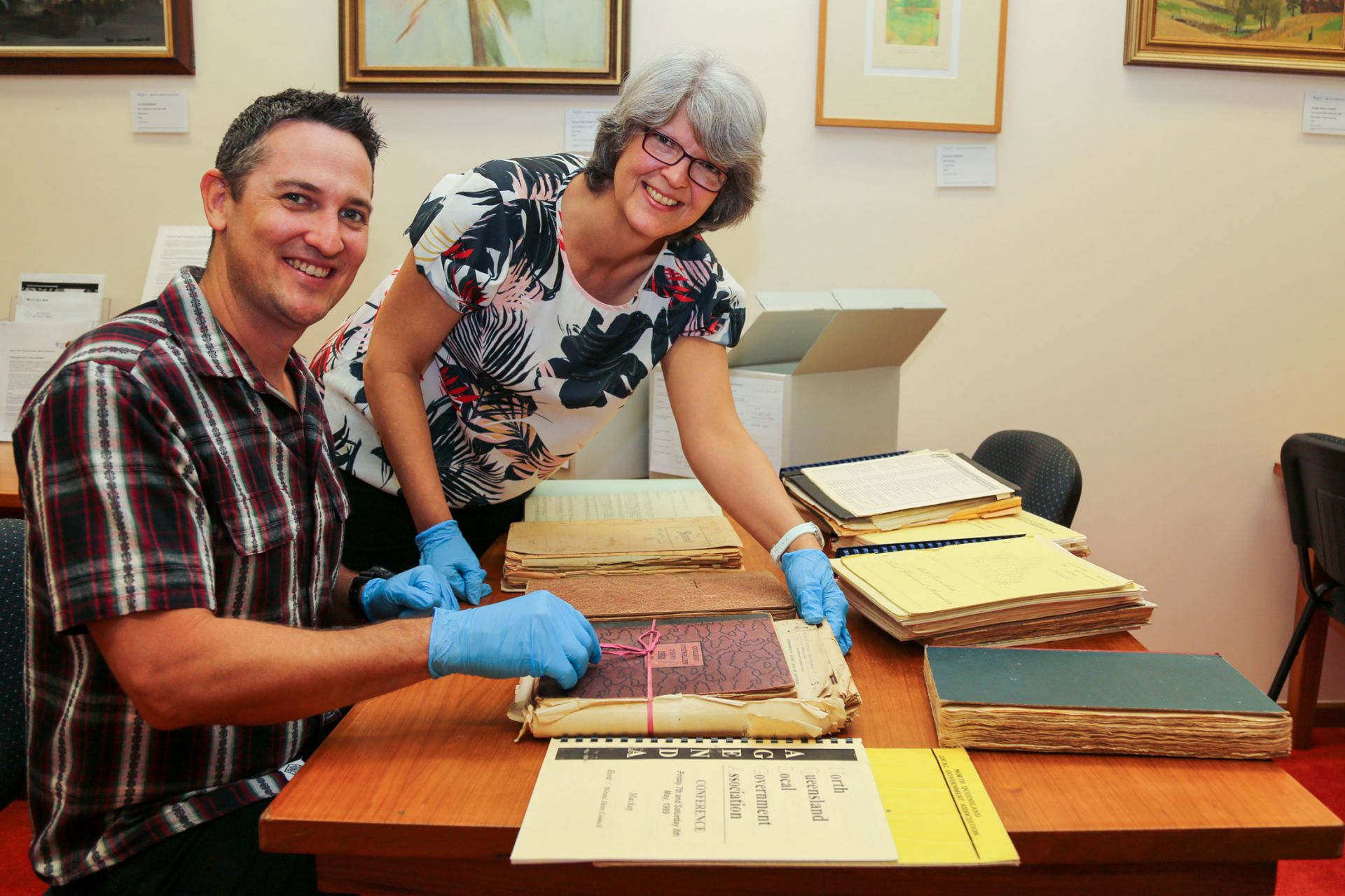 PhD student Patrick White and JCU Library Special Collections Manager Browyn Bronwyn McBurnie look over some of the records, the documents are spread over a table and they are wearing gloves