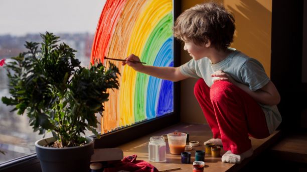 Boy painting rainbow on window