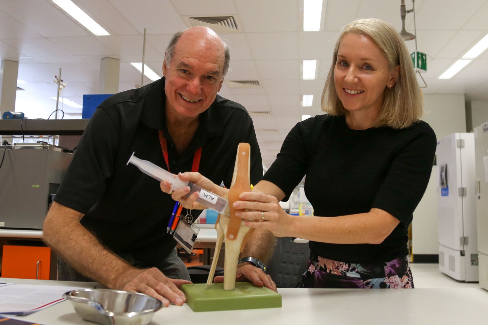 A male and a female pose with a plastic model of a knee joint