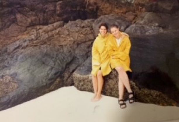 Sonia Solari and Sarah Anderton sitting next to each other wearing raincoats and sitting on large rocks