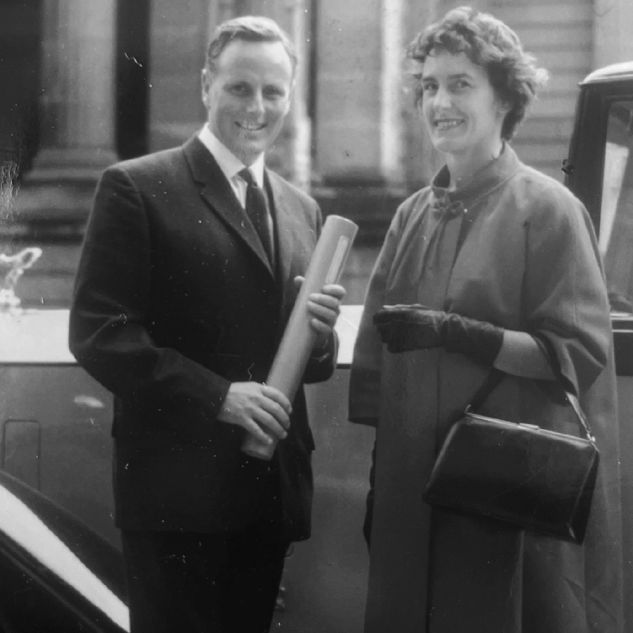 1950s black and white photo of well-dressed couple in front of car
