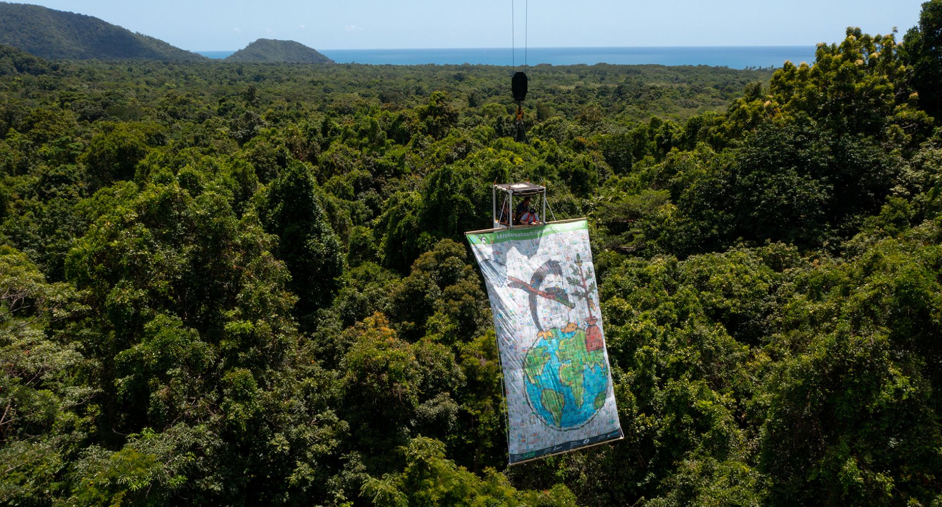 a banner hangs from a crane above the Daintree rainforest