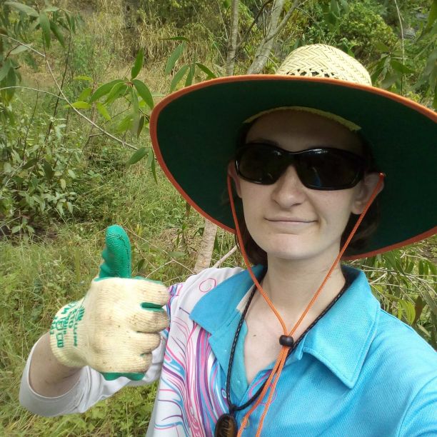 JCU alumni and environmental scientist Merinda Walters smiling with thumbs up wearing a wide brim hat and gloves standing in front of bushland. 