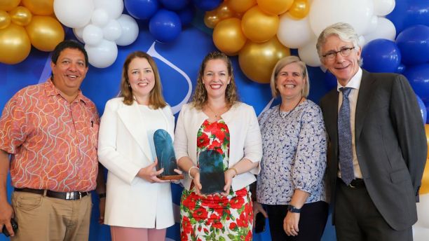 Dr Renee Cremen posing with her Outstanding Alumni award. She is standing in front of a JCU banner, and has two people to her left and two people to her right. 