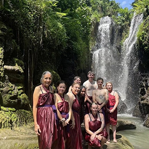 A group of JCU students and staff in traditional Indonesian clothing standing in front of a waterfall