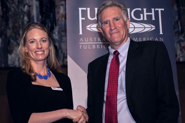 Dr Georgina Gurney shakes hands with a man standing in front of a Fulbright banner