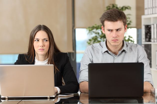 Man and woman look angrily at each other while work at laptops