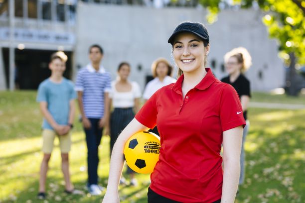 A female sport teacher stands outside with students