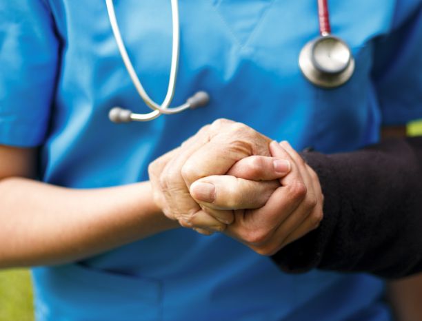 A close-up of a nurse in a blue uniform holding an older person's hand. 