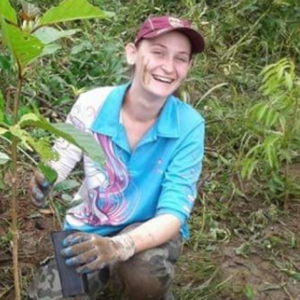 JCU Alumni and environmental scientist Merinda Walters smiling while she crouches and plants a small tree sapling. 