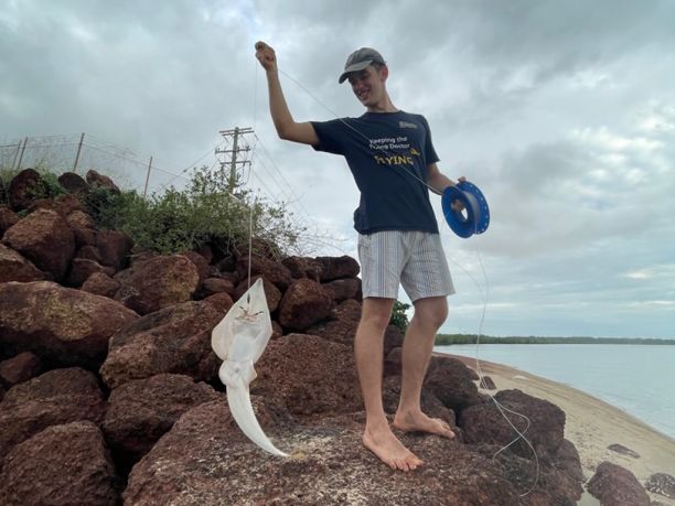 Finley holding up a long, white fish while standing on a rocky jetty. 