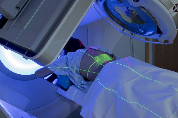 A person lying down with blue and red lights on them and receiving radiation cancer treatment. 