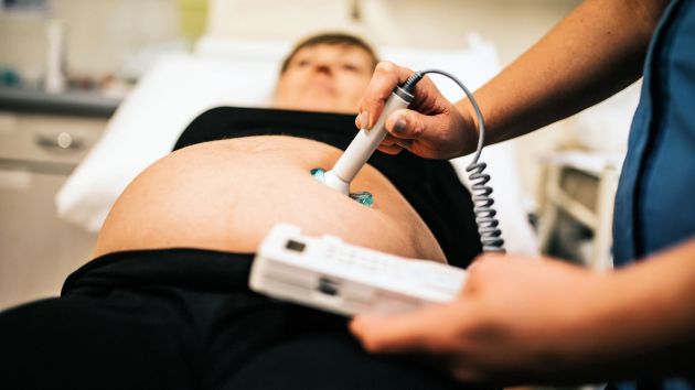 Closeup of person holding ultrasound machine to woman's stomach
