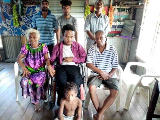 Kingsley Vali sitting in a wheelchair with another six members of his family sitting beside him and standing behind him.