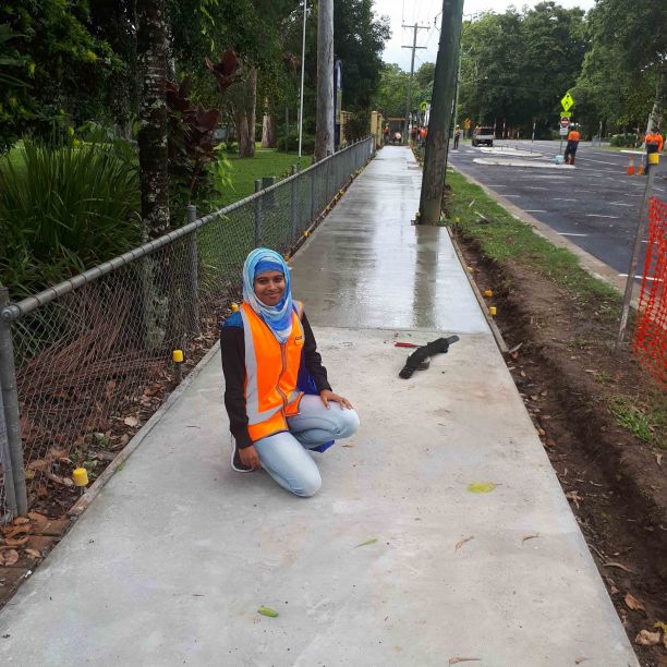 JCU PhD graduate Nafisa Tamanna smiling and kneeling in front of the completed concrete footpath. 