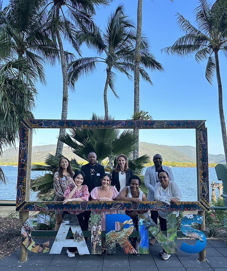 Group of JCU staff and students in front of blue sky and palm trees with a Cairns city sign