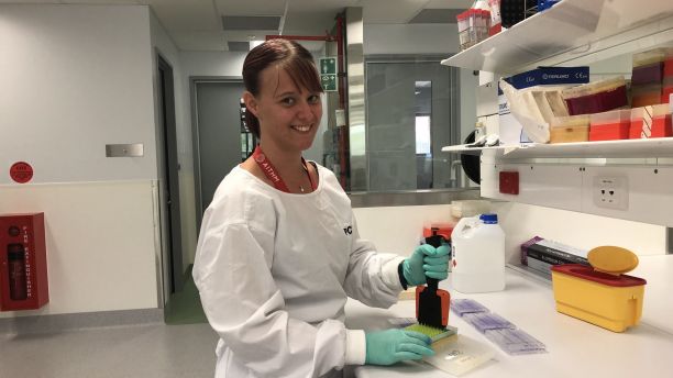 Bachelor of Biomedical Sciences alumni Eva Duck standing at a laboratory bench wearing a lab coat and holding laboratory equipment. 