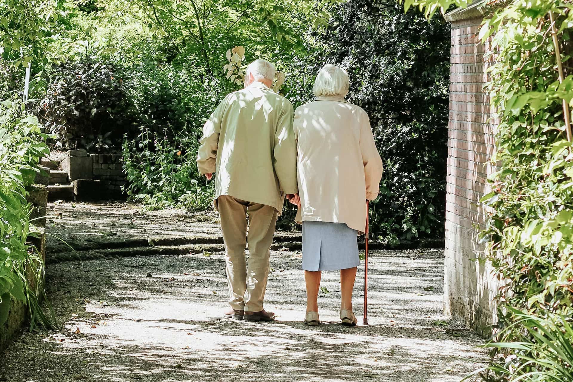 Seen from behind, two elderly people walk down a lane. 