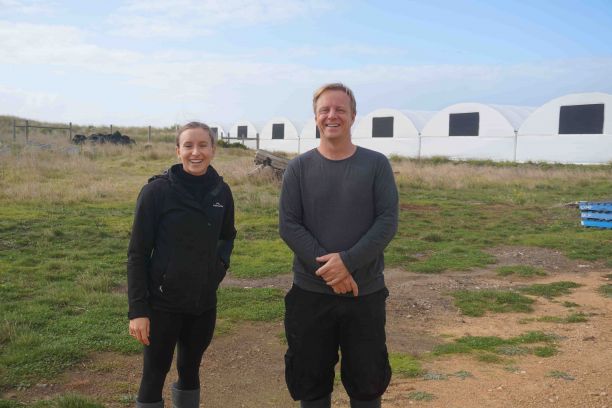 JCU researchers Phoebe Arbon and Kurt Schoenhoff standing together in a small field with large white tents in background stand in