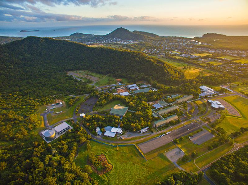 An aerial view of JCU Cairns campus, surrounded by mountains and with the sea in the background. 