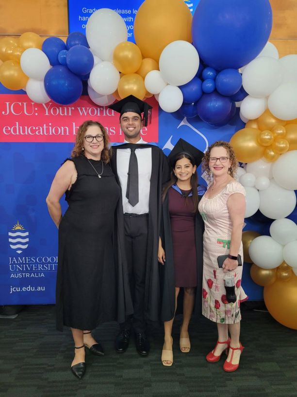 two uni graduates in gowns with two women in front of balloons