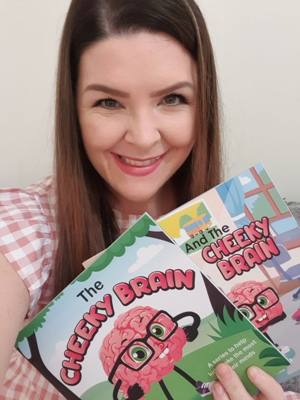 Lauren Cavati smiling while holding up her two books that say the cheeky brain and dane and the cheeky brain. 