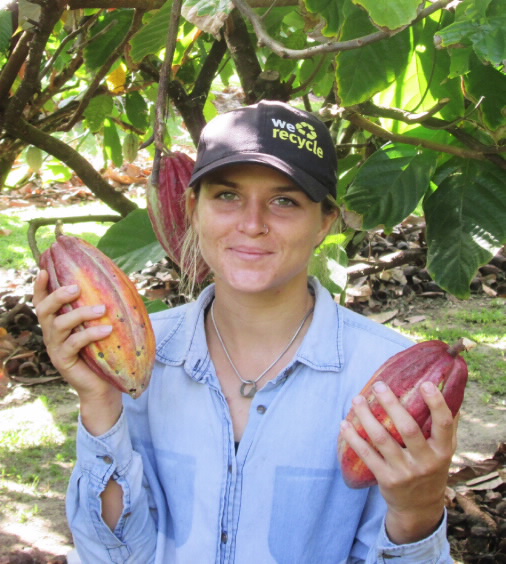 Samantha Forbes holding two cocoa beans in an orchard.  