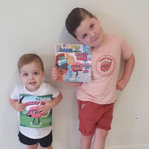 Two young children smile while each holding up a book about the cheeky brain. 