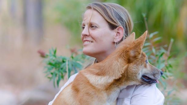 JCU Alumni Shakira Toddy smiling and sitting down with a small tan dingo on her lap looking into the distance. 