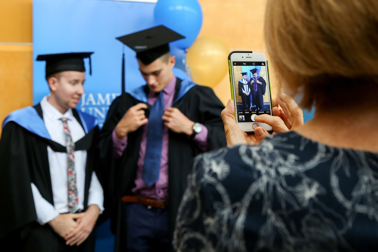Graduands adjust their gowns as someone takes a photo of them