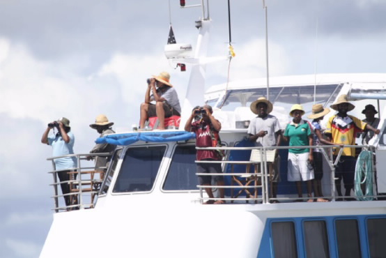 A closer view of the research vessel, with the people on it using binoculars. 