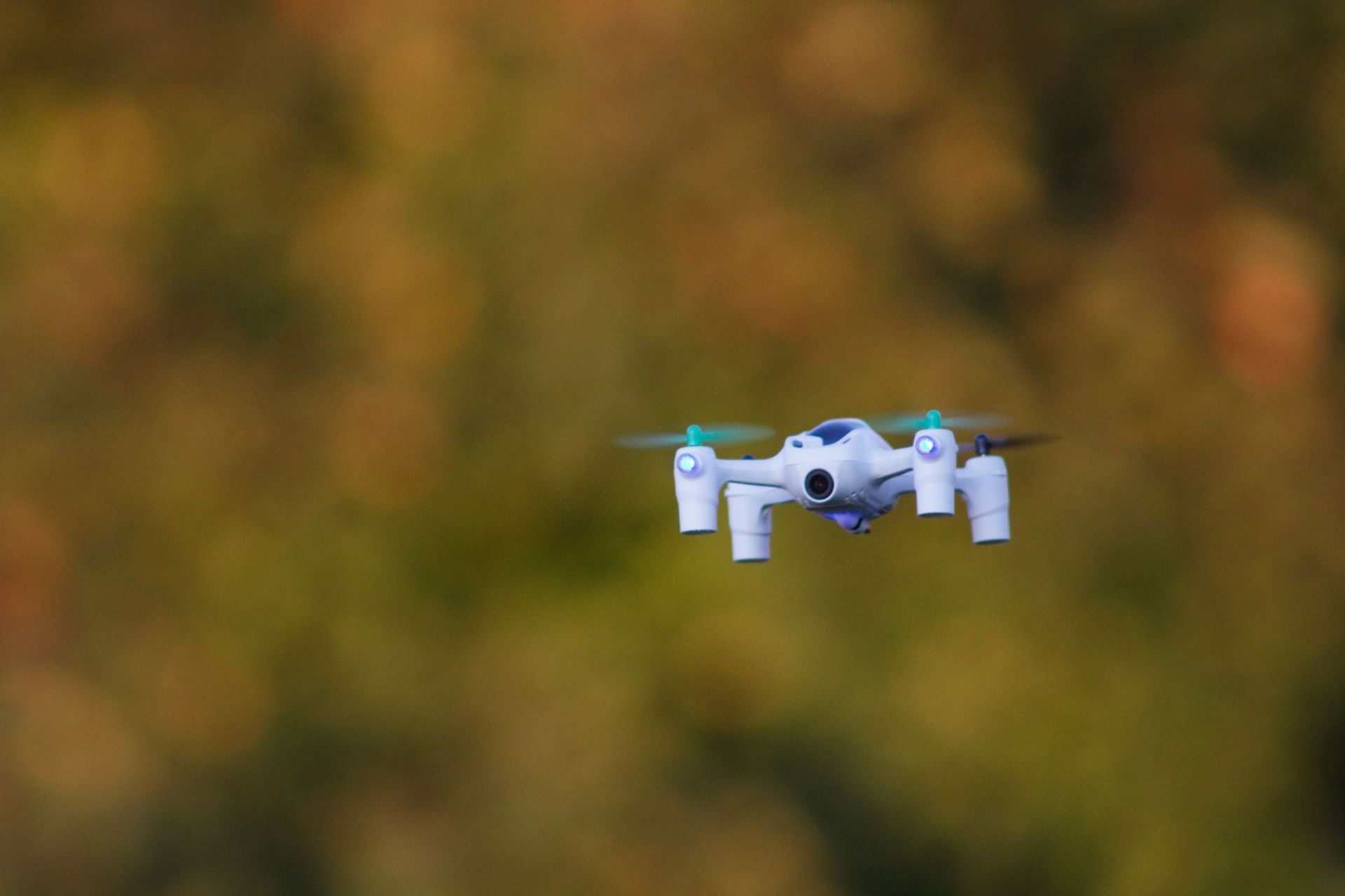A small white drone in focus with a blurred background of orange tones