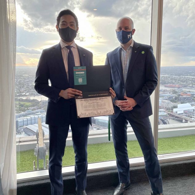 James receiving his Operational Leader of the Quarter award from Ben Nesbitt, the Head of Operations at Meriton Suites. They are on a high level of a building with Sydney cityscape behind them. 