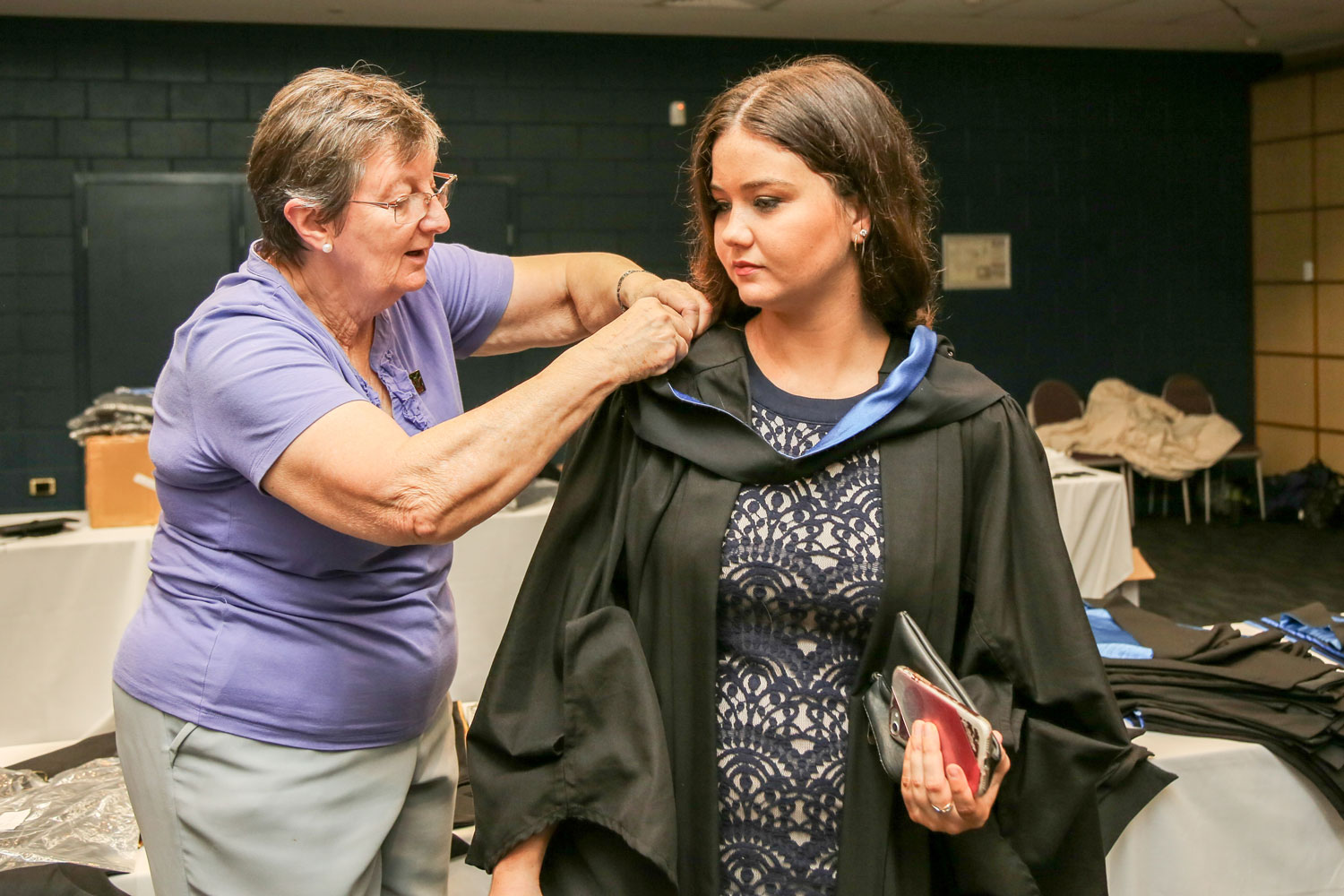 A JCU staff member assists a graduand with her gown