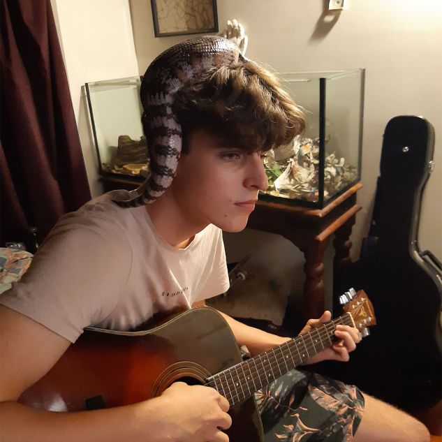 Dr Liz Martin's Son playing guitar with a Lizard on his head