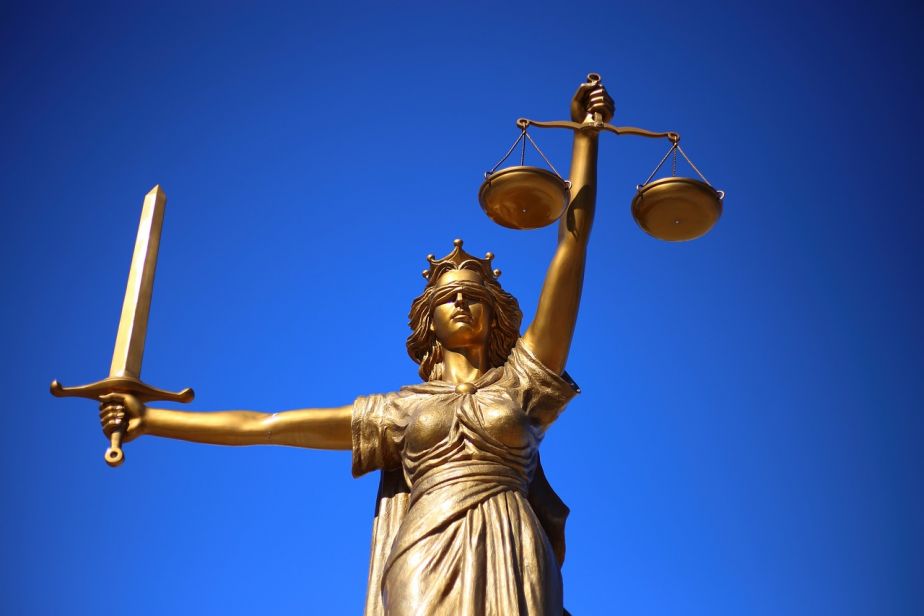 A golden statue of blindfolded Justice holding scales in one hand and a sword in another against a vibrant blue sky