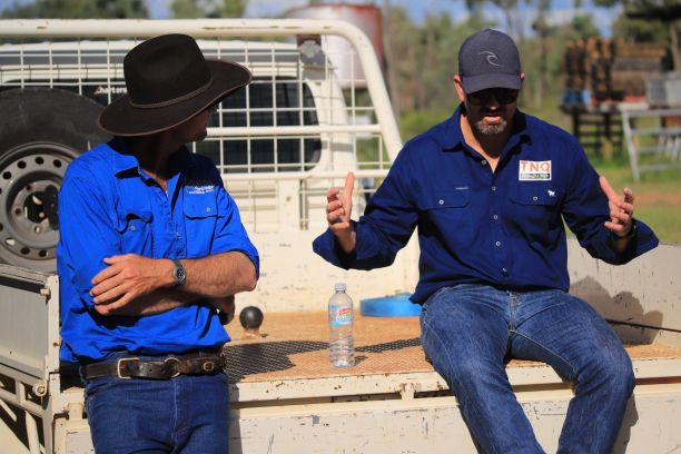 Two farmers sitting in the tray of a white ute. 