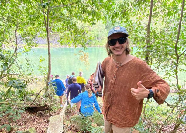 JCU student Indus Fisher smiling with thumbs up in a rainforest with students in the background at a creek. 