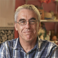 A headshot of Dr Greg Burnett with a maroon background. 
