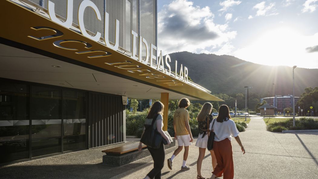 Four students walking out of a building on campus with the sun shining over the mountains.